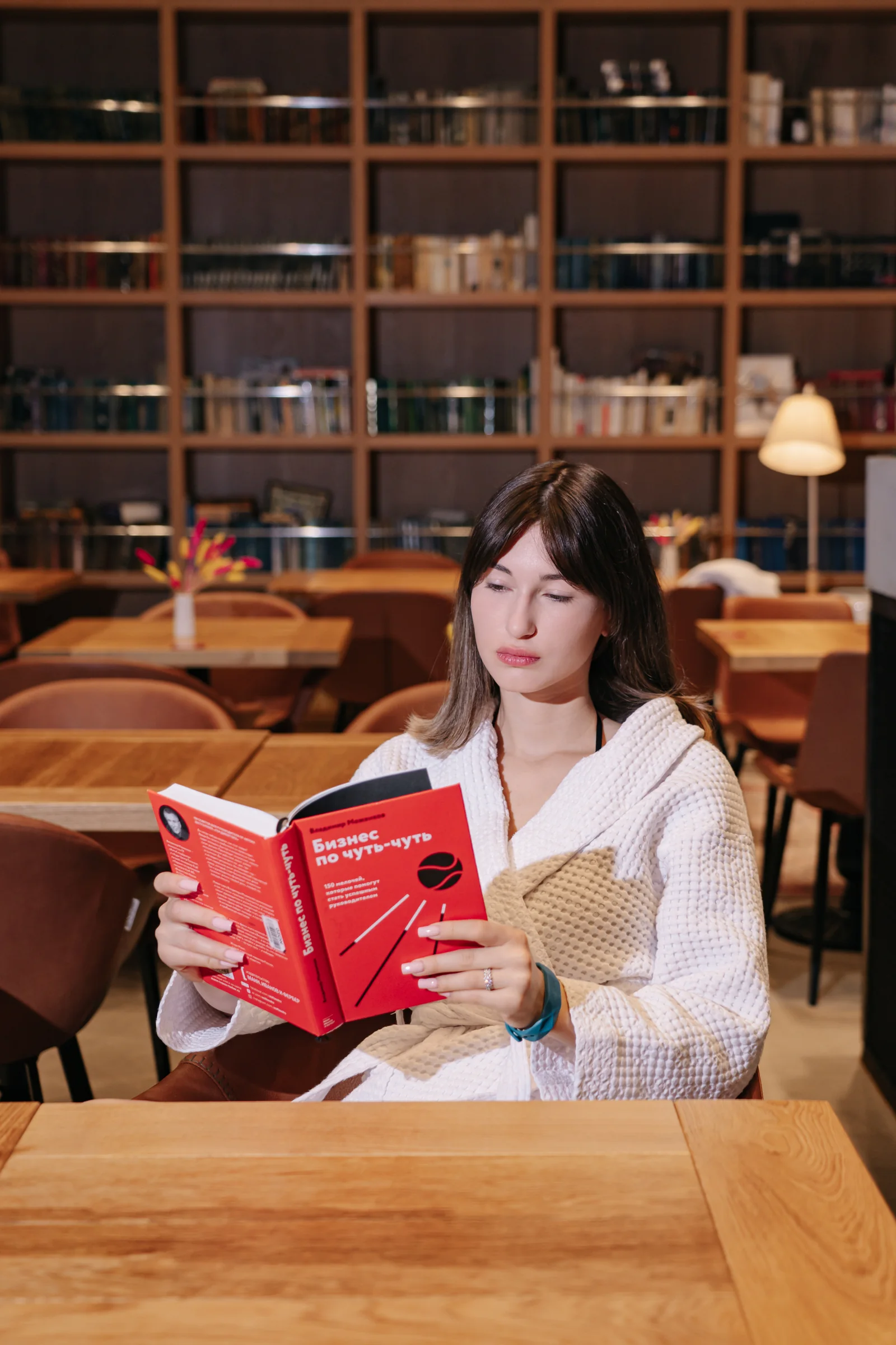 Гостья с книгой в библиотеке GREMM; на фоне книжные стеллажи и теплый интерьер.